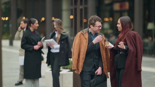 Business professionals engage in a casual conversation while walking in an urban setting. Colleagues discuss work-related topics during a city stroll.