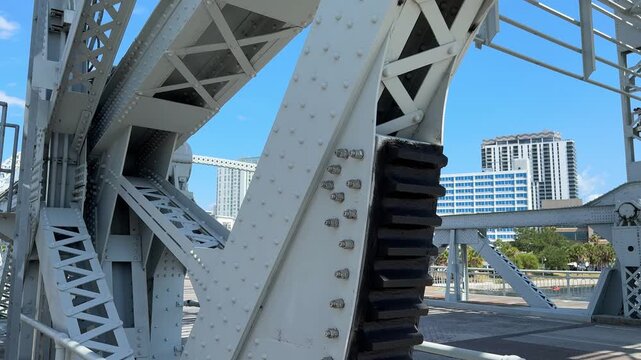 A low angle perspective shows the massive scale of gray steel girders and diagonal supports on an industrial bridge. The intricate pattern of rivets and beams creates a strong architectural presence