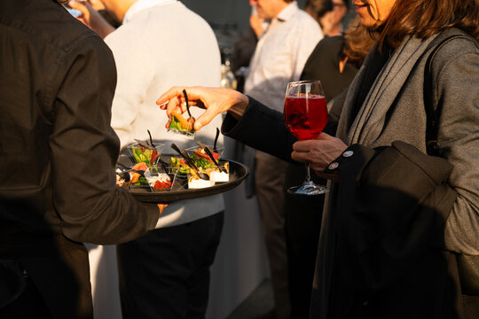 Guests enjoying appetizers and cocktails at a stylish outdoor reception, a server offering canap&eacute;s as people socialize in warm evening light.