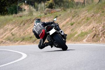 Obraz premium Motociclista con traje de cuero inclinándose en una curva cerrada en carretera de montaña
