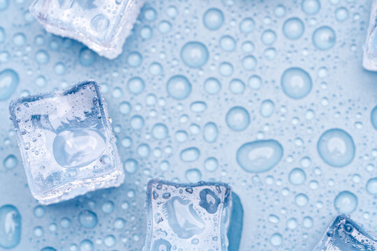 Melting ice cubes with water drops on smooth blue surface