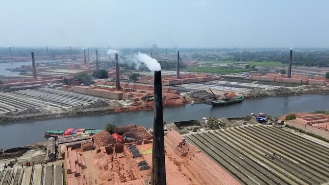 Aerial view of industrial brick kilns with smoking chimneys and workers near a river in Narayanganj, Dhaka Division, Bangladesh.