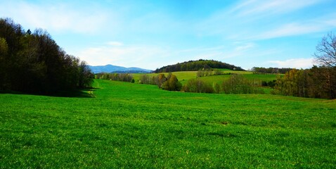 Górska panorama Jesioników z szerokimi łąkami i falującym terenem. Jasne niebo i dobra pogoda tworzą spokojny, otwarty krajobraz pełen zieleni i przestrzeni. © Adam