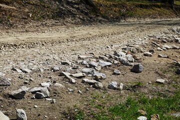 Leśna droga z rozrzuconym kruszywem i większymi kamieniami przy krawędzi. Widoczny etap utwardzania nawierzchni w naturalnym, terenowym otoczeniu. © Adam