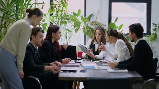 A group of diverse business professionals engages in a collaborative meeting at a modern office table. They are discussing documents and working together on new strategies.