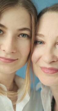 Beautiful mature mother and adult daughter with blue eyes looking at camera close up in the photostudio on blue paper background. Two female generations. Mother's day concept