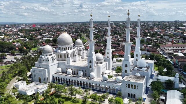 Aerial view of Sheikh Zayed Grand Mosque Solo Surakarta with its white domes and minarets under a cloudy sky in Kecamatan Banjarsari, Jawa Tengah, Indonesia.