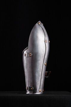 Polished steel vambrace with brass rivets and leather strap, shown in multiple angles against black background, highlighting curves and handcrafted detailing.
