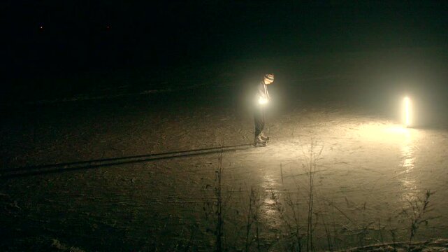 Skater performs jumps. Nighttime icy surface tricks. Skater showcases daring jumps on ice surface. Solitary skater executes impressive jumps on frozen lake under bright lighting