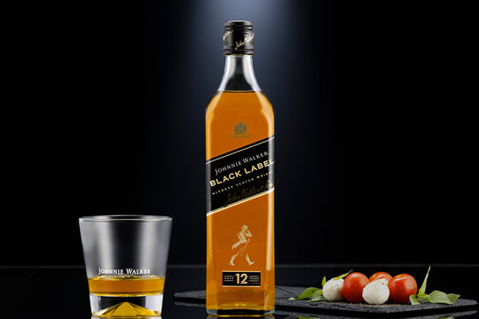 Johnnie Walker Black Label blended Scotch whisky bottle with glass on dark background, styled with gourmet food pairing, illustrative editorial image of premium alcohol concept.
