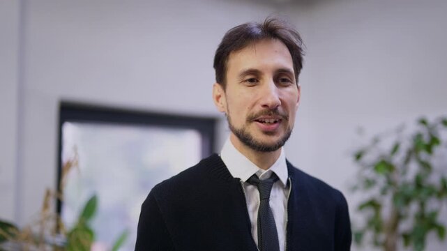 A young business man talks and smiles confidently in a bright, modern office. The confident professional communicates effectively.