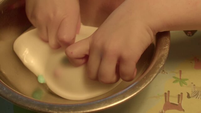 Child hands kneading white slime in metal bowl, sensory squish and stretch, playful tactile exercise, homemade craft therapy, closeup focus on fingers and motion, cleanup empty