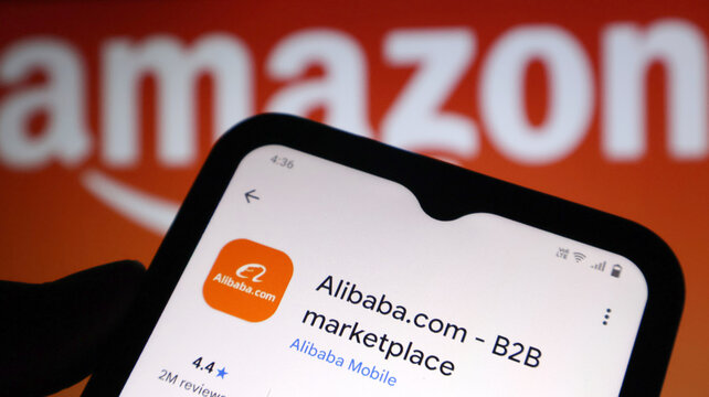 A smartphone displaying the Alibaba marketplace app in front of an Amazon logo