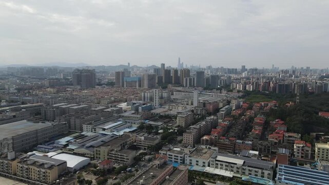 Aerial view of a dense industrial and residential district with factory buildings and distant skyscrapers under a hazy sky in Dongguan, Guangdong Province, China.