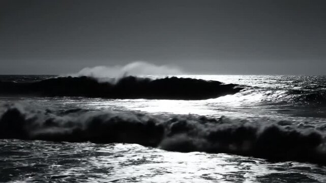 Dramatic ocean waves cresting and breaking silhouetted against a muted, overcast sky, black and white