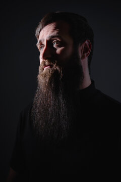 Dramatic portrait of bearded man in dark lighting looking sideways with strong shadows
