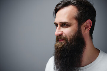 Side profile portrait of a bearded man with long, well-groomed beard and thoughtful expression against neutral gray background, ideal for grooming, fashion,personal branding and editorial use © Loginova