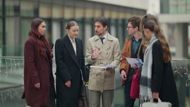 A diverse group of business people engages in a collaborative discussion outdoors in a city setting. They celebrate a successful agreement with high-fives and a unified gesture of achievement.