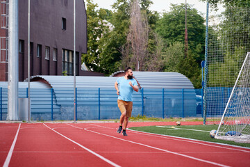 Obraz premium An athlete runs on a red track near a soccer field in an outdoor urban setting, emphasizing health and fitness, surrounded by nature and sports gear, in a motivational and energetic scene.