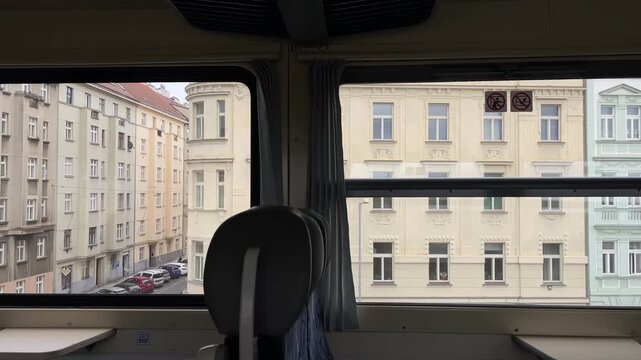 Window view ochre facades passing, empty seat silhouette in foreground, close alignment of apartment blocks, muted palette and urban rhythm, gentle motion blur on glass