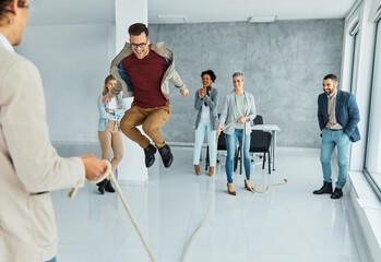 Fototapeta premium Portrait of a group of young business people having fun jumping rope during a meeting in the office. Teamwork and success concept