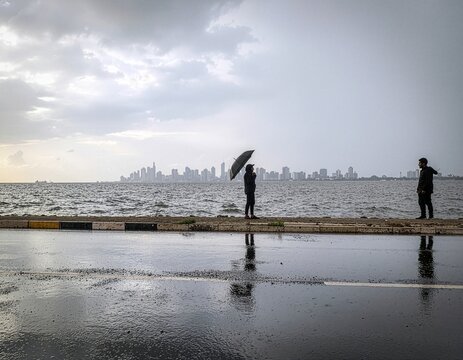 A couple enjoying the rainy season at Marine Drive, Mumbai, with monsoon waves and a wet promenade