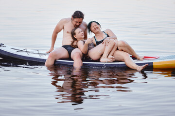 Fototapeta premium A happy family relaxes together on a paddleboard, spending quality time on a serene lake.