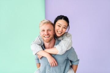 Fototapeta premium Young woman riding on man piggyback laughing by pastel wall