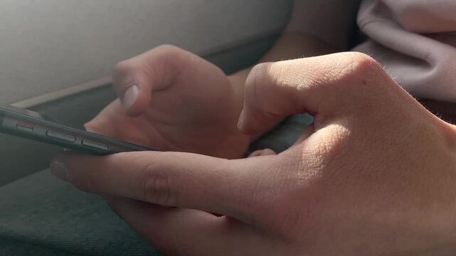 Commuter hands using smartphone onboard transit, seatside window sign visible, closeup touchscreen tapping and scrolling, ambient daylight through cabin, casual passenger