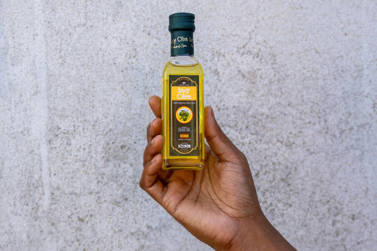 Kishoreganj, Bangladesh - 10 April, 2026 - Close-up of a female hand holding a bottle of Lucy Oliva 100% natural skin care olive oil against a white textured wall.