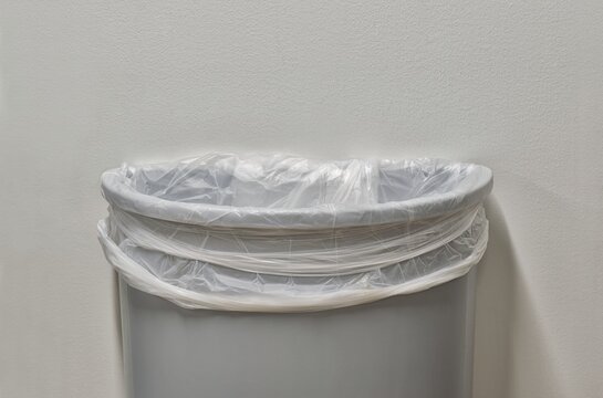 Gray trashcan partial with trash bin liner by white plain wall with copy space.