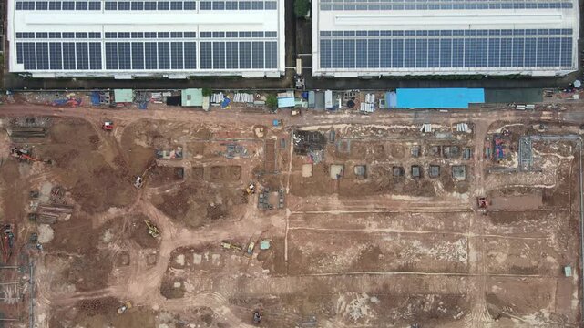 Aerial view of a large construction site with excavators and heavy machinery next to industrial buildings with solar panels in An Phuoc, Dong Nai, Vietnam.