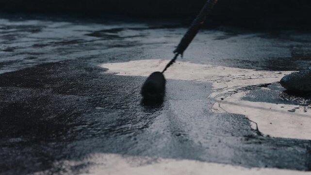 Applying bitumen coating with roller on concrete surface during waterproofing