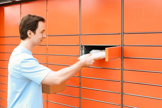 A smiling man picks up his packages from a bright orange automated parcel locker. He holds a cardboard box while retrieving a white envelope. Convenient self-service delivery.