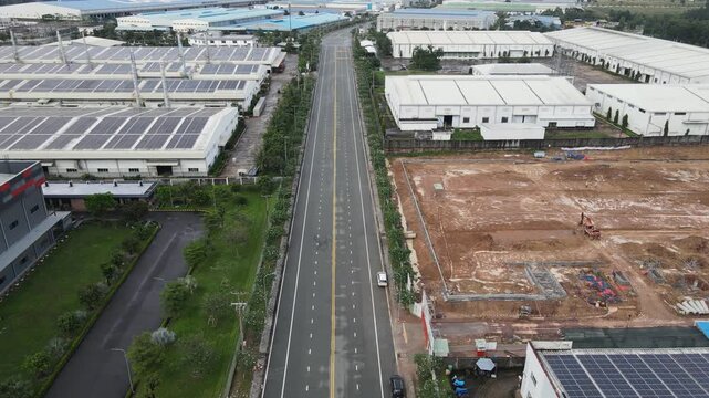 Aerial view of a long straight road passing through an industrial district with solar panels on warehouse roofs and a construction site An Phuoc, Dong Nai, Vietnam.