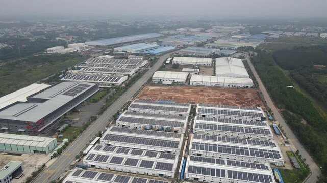 Aerial view of large industrial warehouses featuring extensive solar panel installations on rooftops under a hazy sky in An Phuoc, Dong Nai, Vietnam.