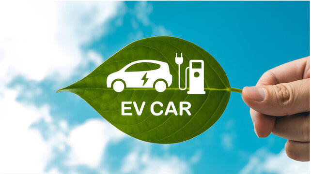 A hand holds a green leaf with an electric car logo under a sunny sky
