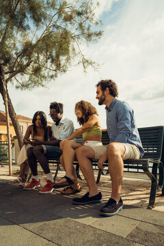 Group of friends sitting on bench looking at smartphone together outdoors