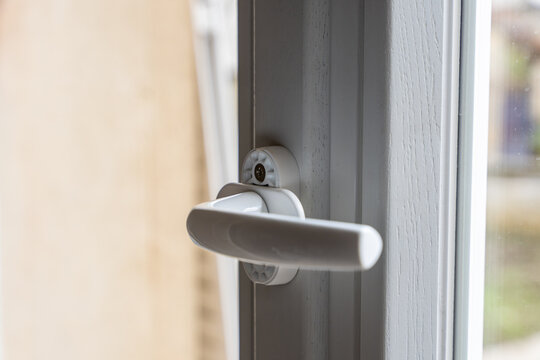 Gros plan sur une poign&eacute;e de fen&ecirc;tre moderne en PVC blanc, symbole d'une installation ou d'une r&eacute;novation r&eacute;ussie, avec un escabeau &agrave; proximit&eacute; &eacute;voquant les derni&egrave;res finitions int&eacute;rieures.