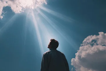 Man Gazing Upwards at Sunbeams Breaking Through Clouds. © Sitti