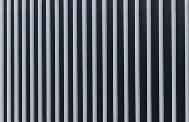 Obraz premium Vertical metal facade with repeating light and dark stripes. Modern building exterior detail with abstract architectural pattern. Suitable for