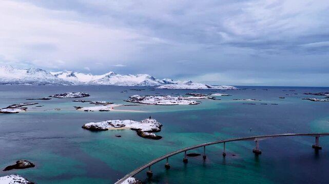 Drohne schwenkt &uuml;ber schneebedeckte Inseln mit Br&uuml;cke und t&uuml;rkisfarbenem Meer in Nordnorwegen