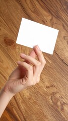 Obraz premium female hand holding a blank white business card against a natural dark wood background, mockup for brand identity, professional networking, communication