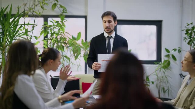 A male business professional leads a discussion, presenting financial charts to his colleagues. The team actively participates in a productive office meeting.