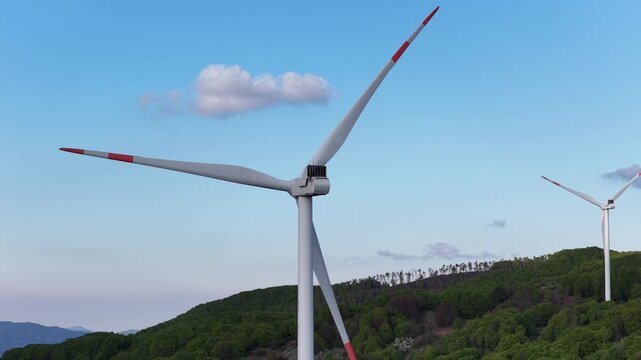 Aerial view of wind turbines at Passo Di Cento Croci with green hills and blue sky in Varese Ligure, Liguria, Italy.