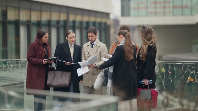 A diverse group of professional business people actively review documents and discuss ideas outdoors. This dynamic team collaborates on a project in an urban setting.