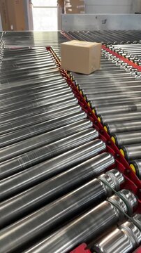 Vertical stock video conveyor rollers parcels gliding through stainless lanes with red rails, mixed items including padded envelope, polybag, cardboard box pass through automated