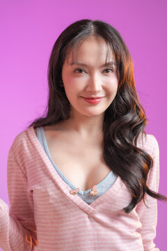 beautiful young East Asian woman with long wavy dark hair and a bright toothy smile, looking away and laughing. She is wearing a soft pink striped top with a light blue inner layer, set against a vibr