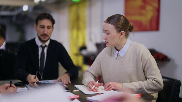 A professional business team engages in a productive meeting within a modern office setting. Young colleagues collaborate, exchanging documents and ideas during their work session.