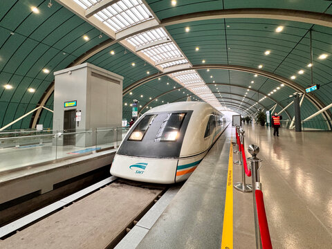 Shanghai Maglev Train (SMT) at Longyang Road station platform, the world's fastest commercial magnetic levitation train in China. Futuristic curved green tunnel station interior with sleek white high-